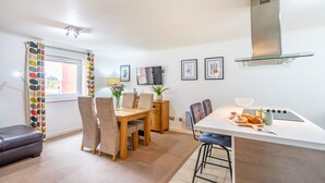 A modern kitchen with a large island, a dining area with chairs, and a TV on the wall.