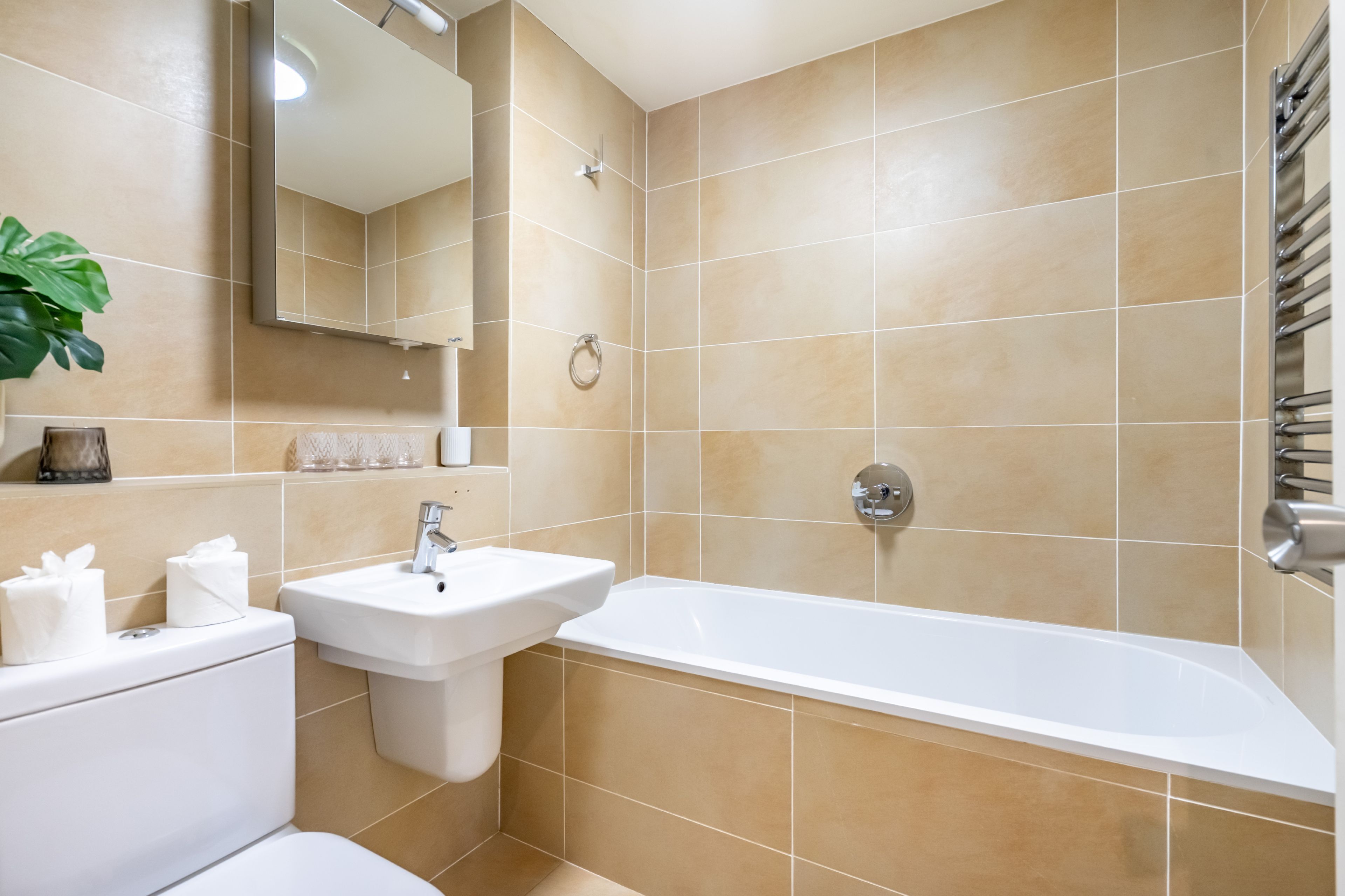 Ein Badezimmer mit beigen Fliesen, einem weißen Waschbecken, einem Spiegel, einer Toilette und einer Badewanne.