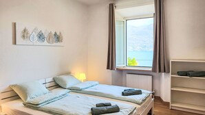 Ein Zimmer mit zwei Betten, einem Fenster mit Blick auf ein Gewässer, einem Heizkörper und einem Regal mit Handtüchern.