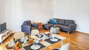 Ein modernes Wohnzimmer mit einer Couch, einem Esstisch mit Tellern, Tassen und einer Obstschale.
