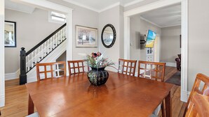 A dining area with a wooden table, chairs, a vase with flowers, a framed picture, and a mirror on the wall. - 3br 2ba hse  AC WiFi 3 blks to Xcel Event Center, dining,&bars 6.8 mls to airprt (Saint Paul)