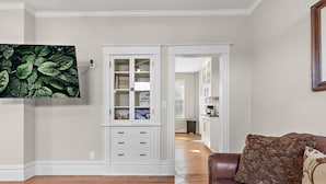 A living room with a brown leather couch, a flat-screen TV mounted on the wall, and a white cabinet with drawers. - 3br 2ba hse  AC WiFi 3 blks to Xcel Event Center, dining,&bars 6.8 mls to airprt (Saint Paul)