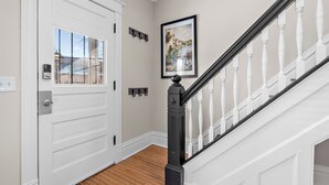 A hallway with a white door, a wooden floor, a black staircase railing, and a framed picture on the wall. - 3br 2ba hse  AC WiFi 3 blks to Xcel Event Center, dining,&bars 6.8 mls to airprt (Saint Paul)