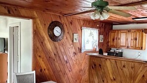 Interior em madeira com mesa e cadeiras de jantar, cozinha e ventilador de teto.