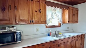 Uma cozinha com armários de madeira, micro-ondas, pia e janela com cortina estampada.