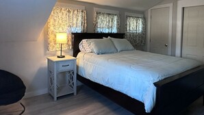 Quarto com teto inclinado, uma cama, mesa de cabeceira com abajur e um guarda-roupa.