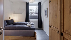 Une chambre à coucher comprenant un lit, une armoire, une fenêtre avec des rideaux et un luminaire suspendu.