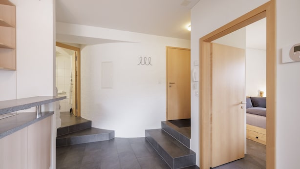 Un intérieur moderne avec un comptoir de cuisine, un revêtement de sol en carrelage gris, une porte en bois et un escalier menant à une autre pièce.
