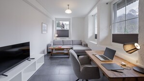 Un salon moderne comprenant un téléviseur à écran plat, un canapé, une table basse, un bureau avec un ordinateur portable et une lampe.