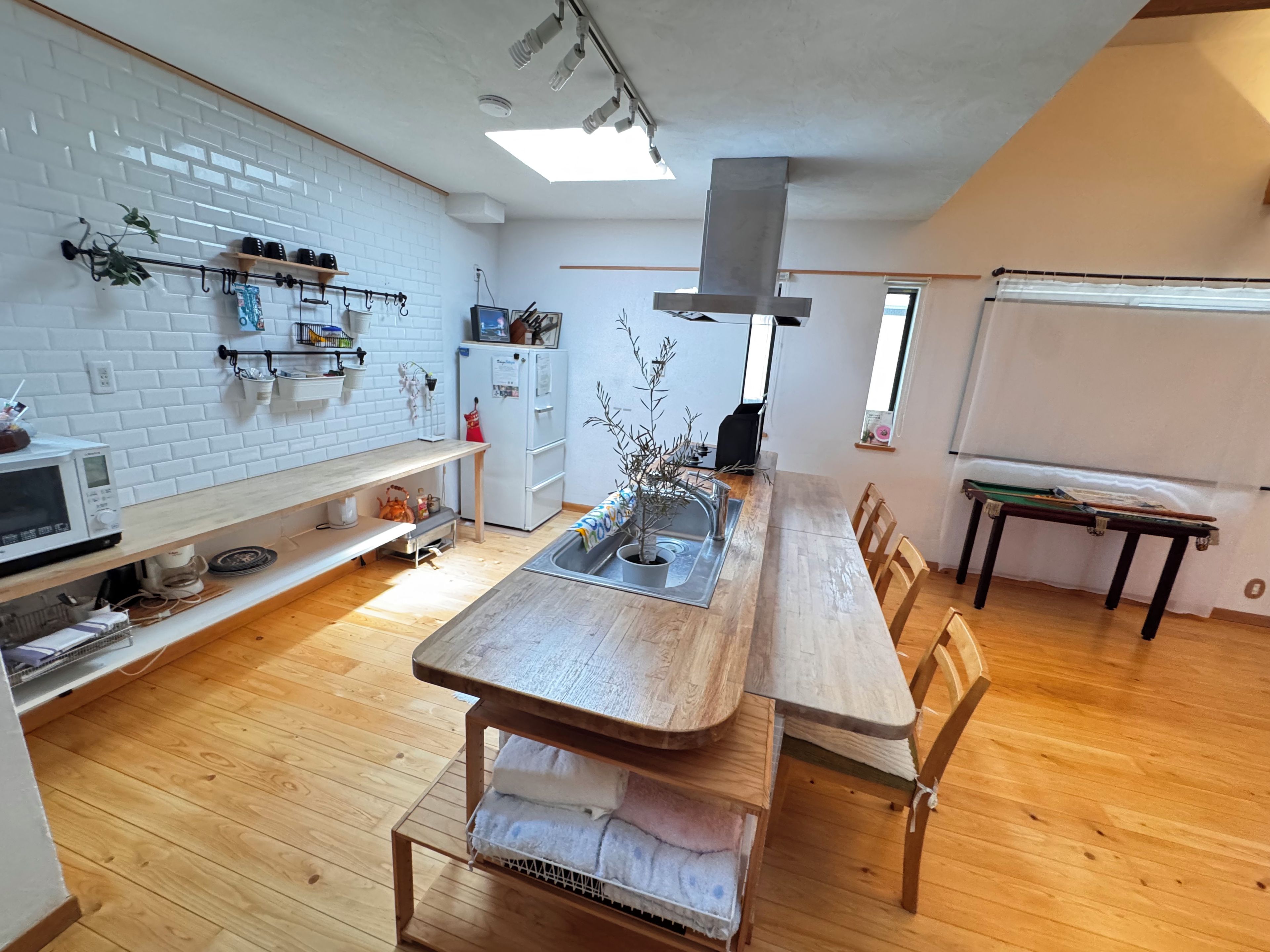 A modern kitchen with a wooden dining table, white brick backsplash, and a whiteboard.