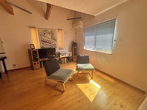Una sala de estar con piso de madera, televisor, parlantes y dos sillones.