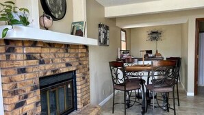 A living room with a brick fireplace, a dining table with chairs, and a chandelier.