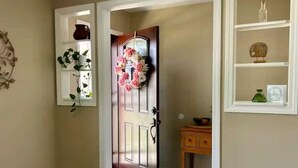 A hallway with a wooden door, a small wooden table, and a shelf with decorative items.