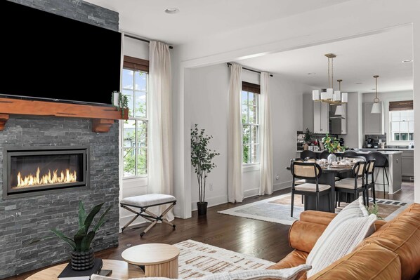 A modern living room with a fireplace, a dining area, and a kitchen.