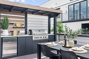 An outdoor kitchen with a grill, dining table, and chairs. - The High Note - Spectacular rooftop, walk to Gulch (Nashville)