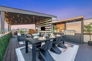 An outdoor dining area with a grill, seating, and string lights.