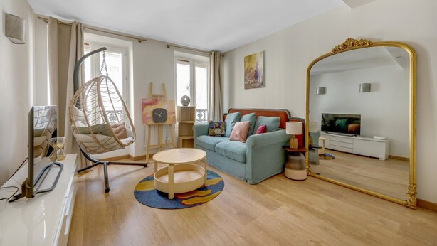A modern living room with a hanging chair, a sofa, a round coffee table, and a large mirror.