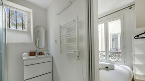 A small, bright room with a white dresser, a mirror, a radiator, and a bed with a view of a balcony.