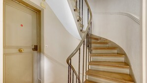A spiral staircase with wooden steps and metal railings, leading to a beige door with a brass doorknob and a red 'B' marking.