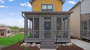 A covered porch with a door and steps leading up to it, surrounded by a landscaped garden with rocks and a small lawn. - Fun In The Sun â€“ A Bright andBreezy Getaway in Navvy Town (Ottawa)