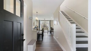 A hallway with a dark door, a staircase, and a dining area with chairs and tables. - Fun In The Sun â€“ A Bright andBreezy Getaway in Navvy Town (Ottawa)