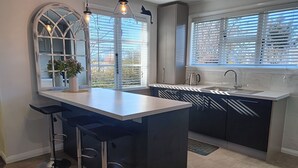 A modern kitchen with a central island, bar stools, a large window with blinds, and pendant lighting. -  Country Cottage Delight in the Hurunui.
(Spotswood/Cheviot)
 (Spotswood)