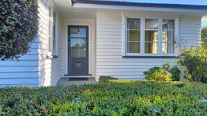 A house with a dark front door, white siding, and a window with a view of the outdoors. -  Country Cottage Delight in the Hurunui.
(Spotswood/Cheviot)
 (Spotswood)