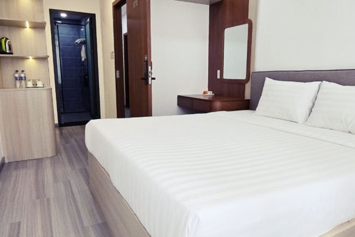 A hotel room with a large bed, a wooden wardrobe, a small desk, and a mirror on the wall.