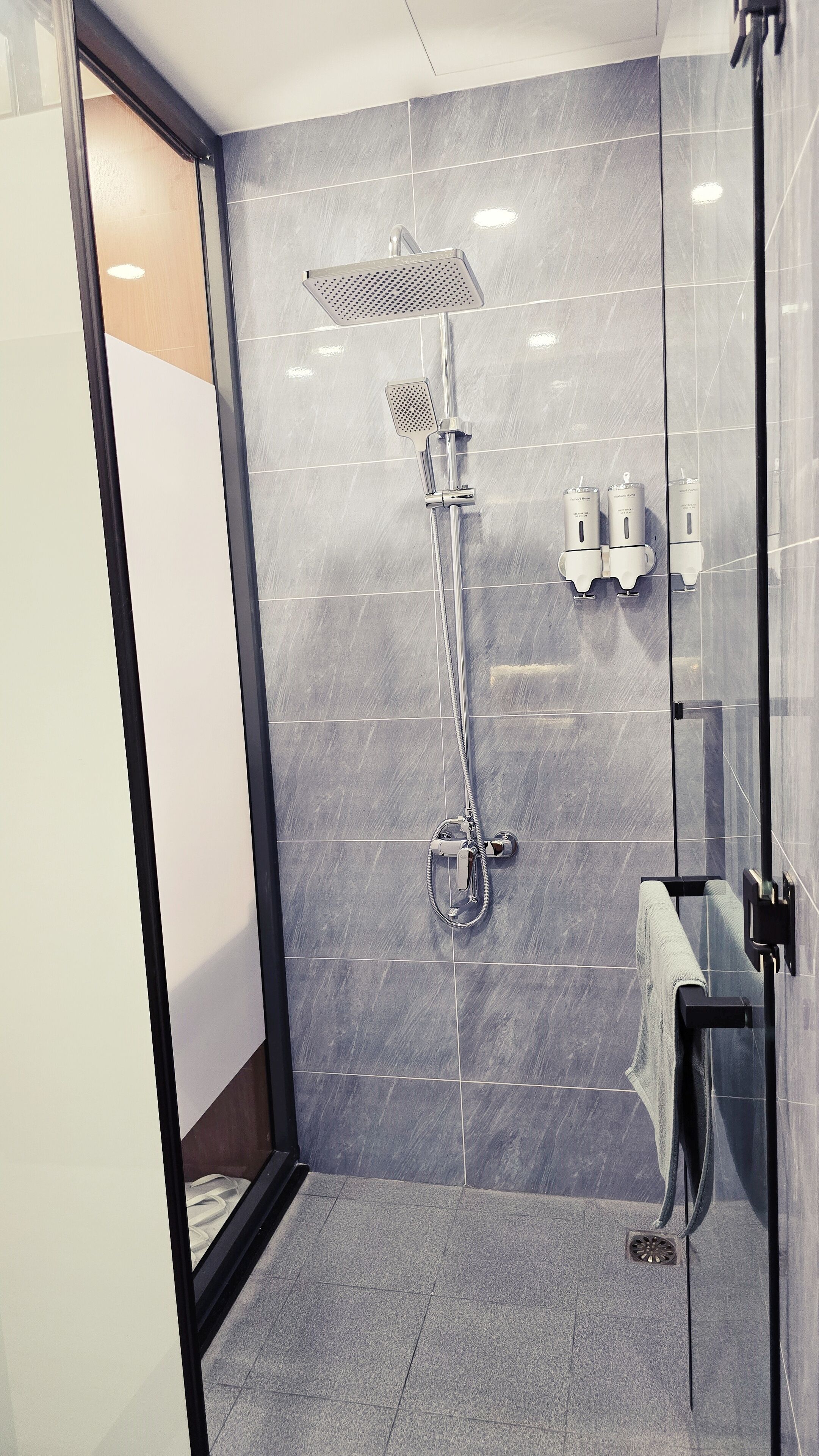 A modern bathroom with a glass shower enclosure, a handheld showerhead, and a towel rack.