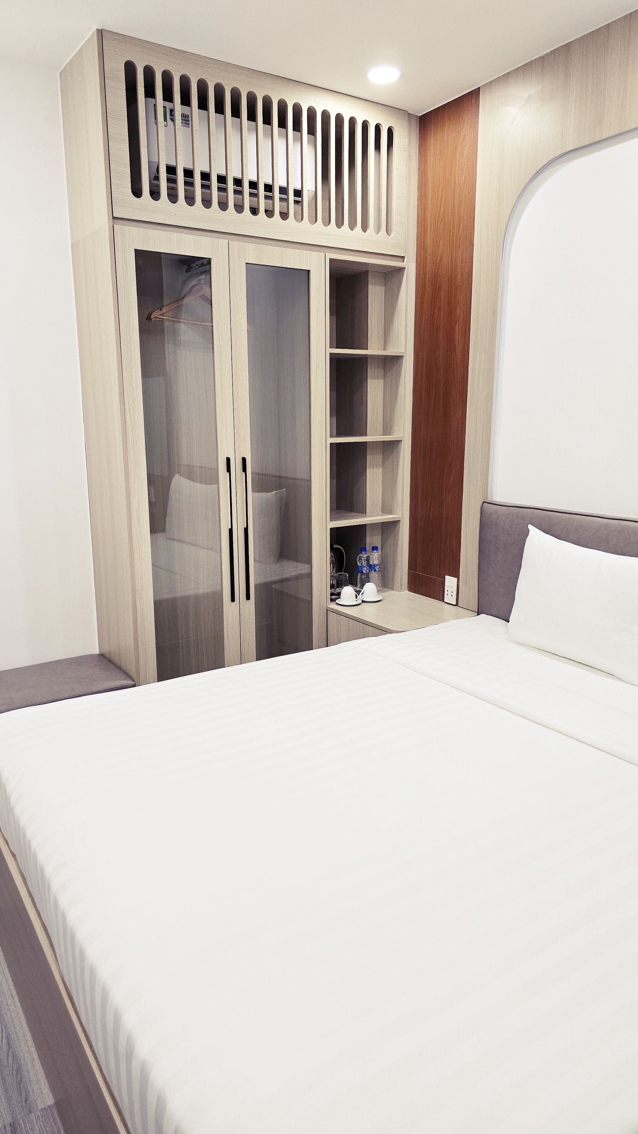 Una habitación de hotel con una cama grande, un armario con espejo y una mesita con dos botellas.
