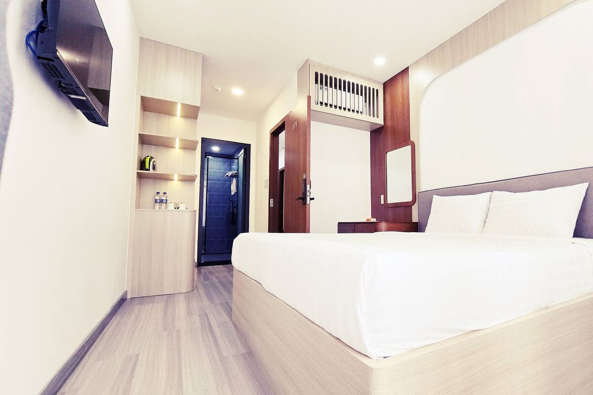 Une chambre d’hôtel moderne dotée d’un grand lit, d’un téléviseur intégré, d’un petit bureau avec une chaise et d’un espace douche.