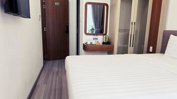 Ett hotellrum med en stor säng, en tv som är monterad på väggen, en garderob med en spegel och ett litet bord med toalettartiklar.