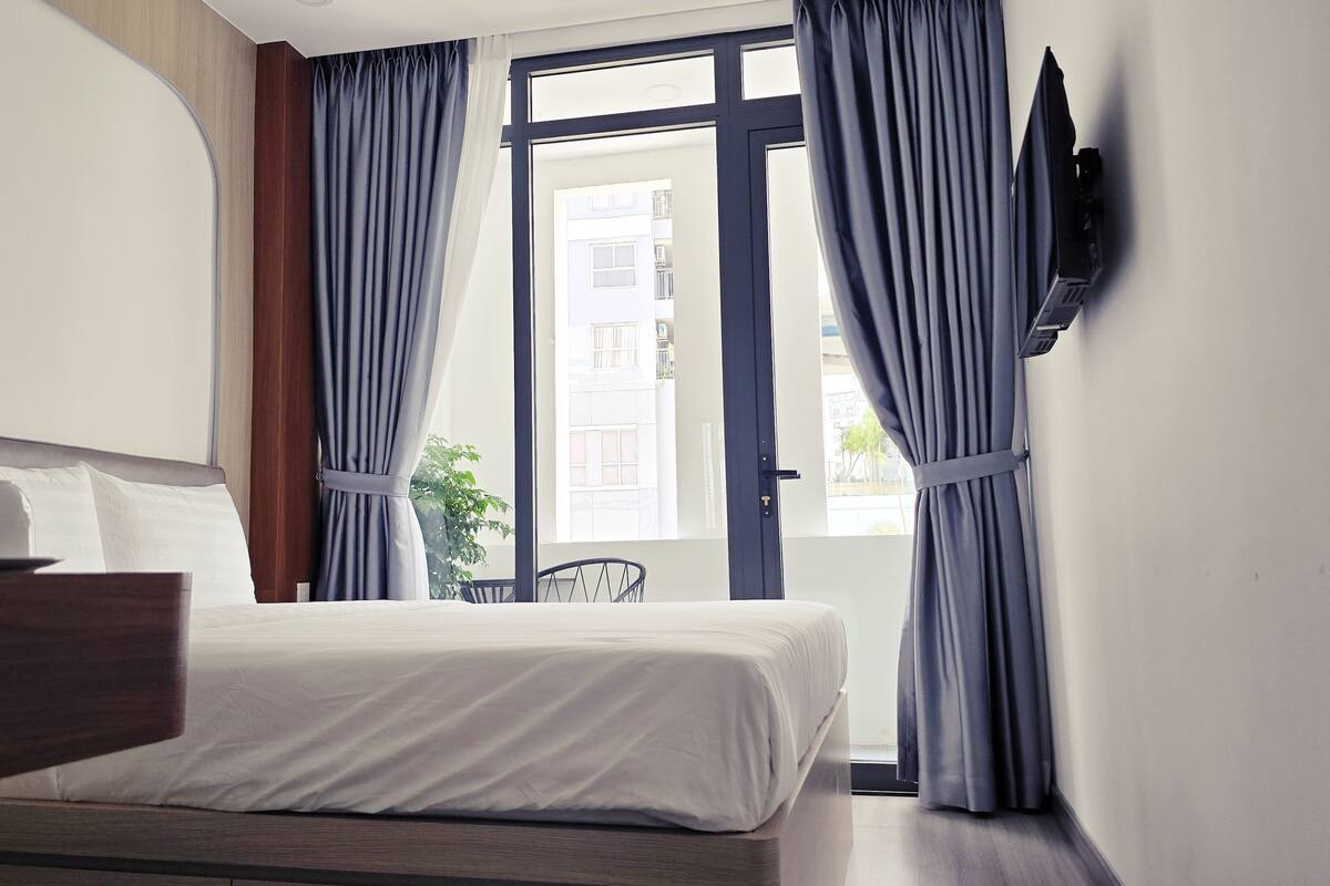 Une chambre d’hôtel équipée d’un lit, d’un bureau, d’une chaise, d’un téléviseur fixé au mur et d’une fenêtre avec des rideaux.
