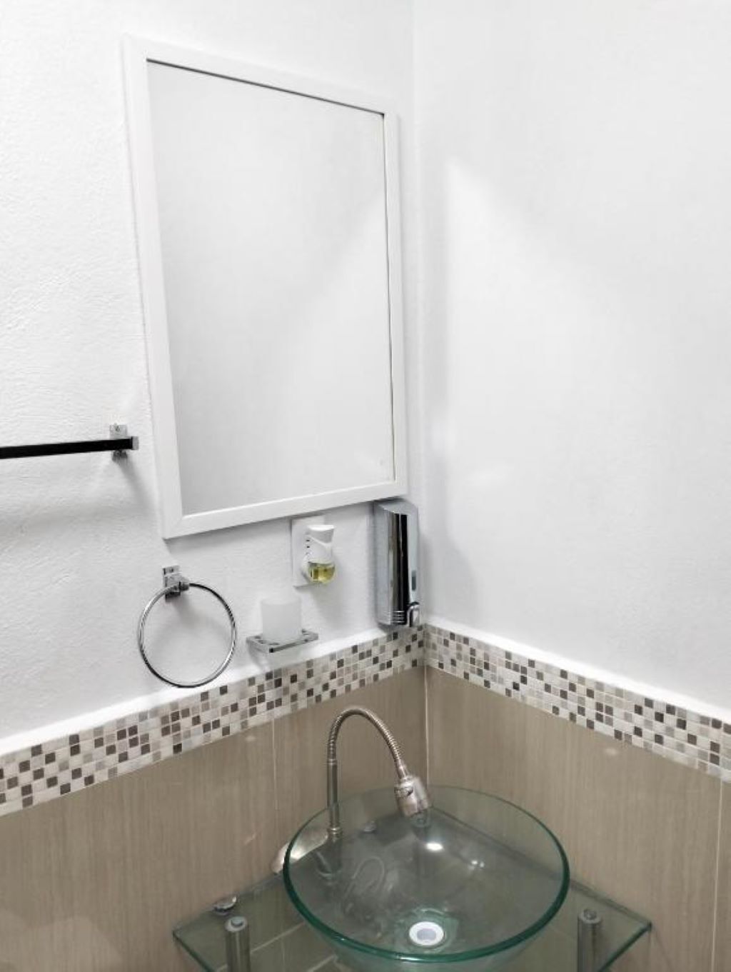 A bathroom with a glass sink, a towel rack, a toilet paper holder, and a mirror.
