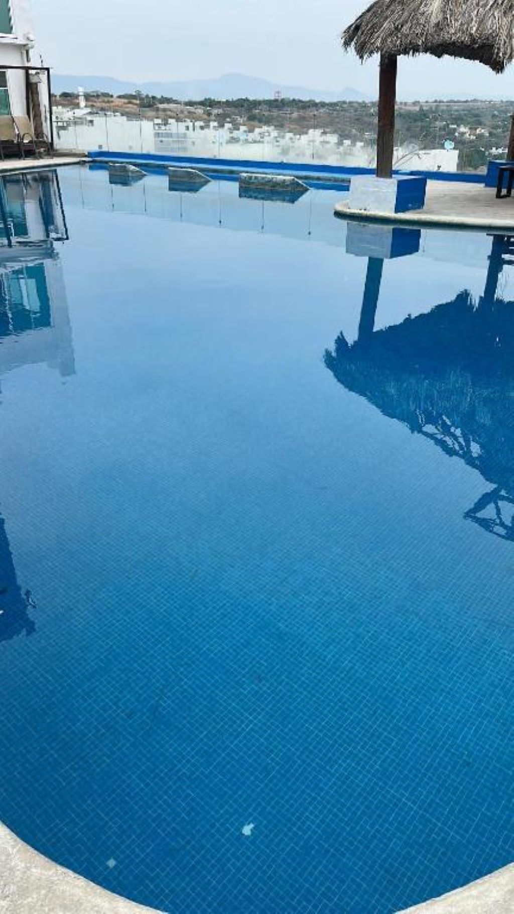 Een helderblauw overloopzwembad met uitzicht op verre gebouwen en bergen.