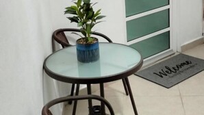 Un tavolo rotondo in vetro con una pianta in vaso, due sedie in vimini e un tappetino di benvenuto.