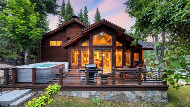 A wooden cabin with a hot tub, deck, and stone foundation.
