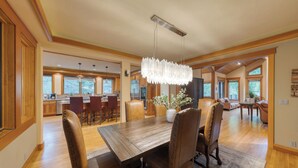 A spacious dining area with a wooden table and leather chairs, a chandelier, and a view of the kitchen and living room.