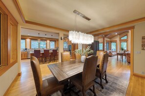 A spacious dining area with a wooden table and leather chairs, a chandelier, and a view of the kitchen and living room.