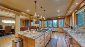 A modern kitchen with a large island, wooden cabinets, and pendant lighting.