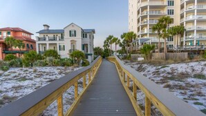 A wooden boardwalk leading to a beachfront area with buildings on either side.