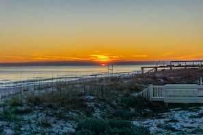 Eine Strandlandschaft mit Sonnenuntergang, einer Holzstege und einem eingezäunten Bereich.