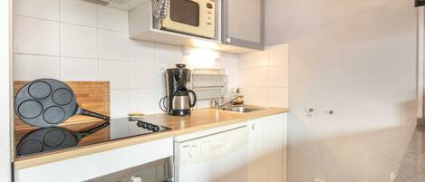 A compact kitchen with a microwave, coffee maker, and a wooden cutting board.