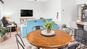 A modern living room with a sofa, a coffee table, and a TV. There is a dining table with chairs and a ceiling fan. - Cottage by the Lake, 1 bedroom full size house, full kitchen, 2 living areas.  (Long Jetty)