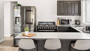 A modern kitchen with a central island, stainless steel appliances, and dark cabinetry. - Cottage by the Lake, 1 bedroom full size house, full kitchen, 2 living areas.  (Long Jetty)