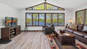 Ein geräumiges Wohnzimmer mit großem Fenster, Deckenventilator, Ledersofa und Fernseher auf Holzständer.