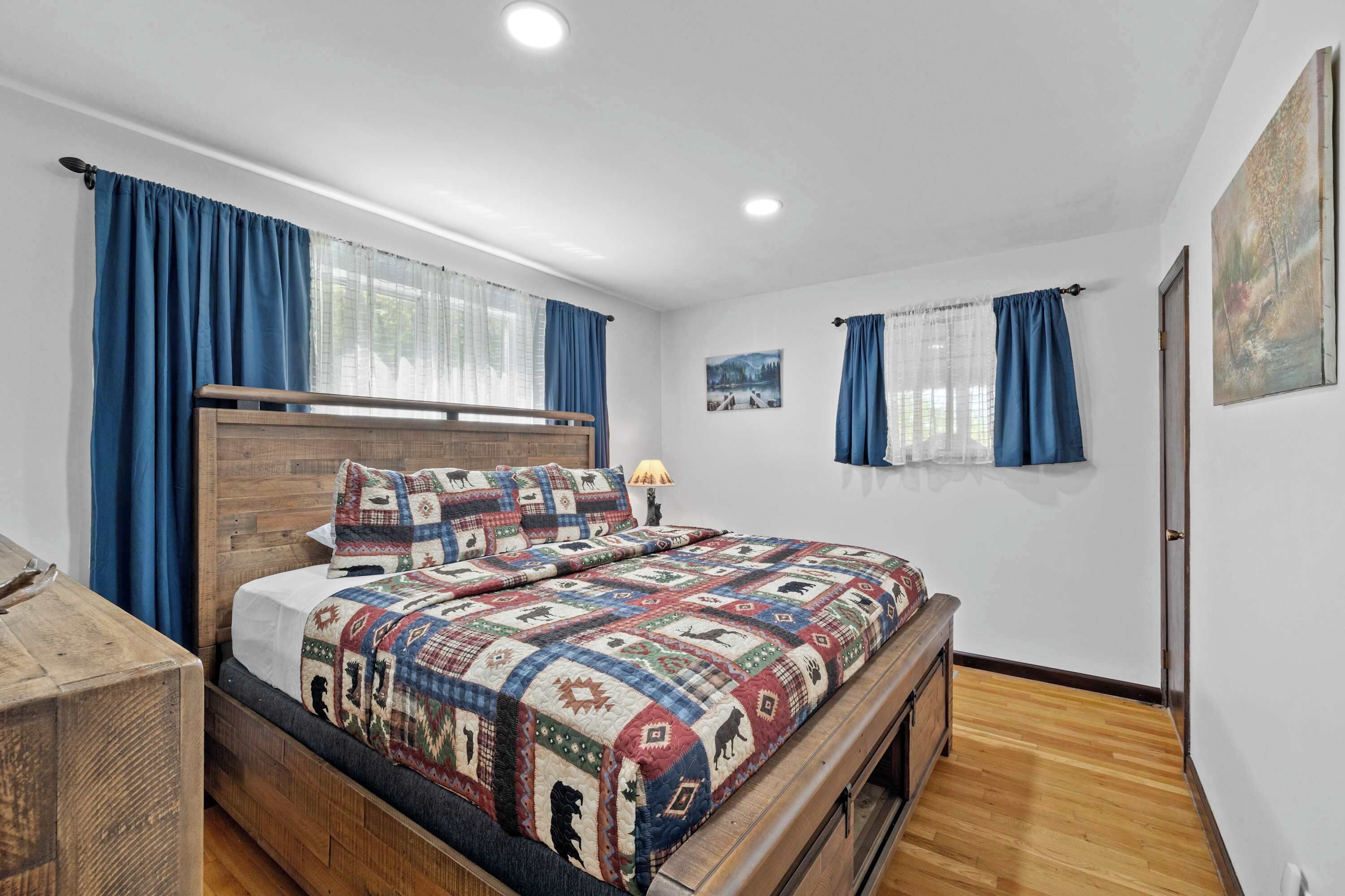Une chambre à coucher avec un lit en bois, des rideaux bleus, une table de chevet et un tableau accroché au mur.