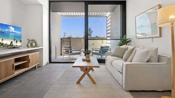 Un salon moderne avec un téléviseur, un canapé, une table basse et un balcon offrant une vue agréable.