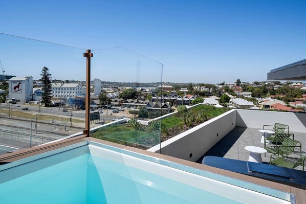 A rooftop pool with a clear view of a residential area and a building with a kangaroo logo.