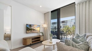 A modern living room with a large window, a flat-screen TV, a round coffee table, and a sofa.